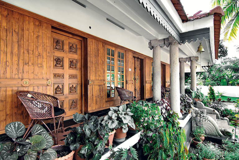 A modern house in Kerala designed on the features of a traditional nalukettu, with a courtyard inside. The main door latch is in the old style but newly made, as well as the surface decoration of another door.
